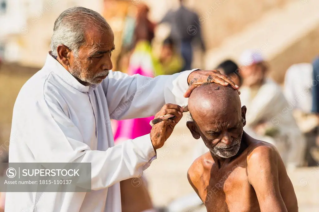 India, Uttar Pradesh, Banaras, Barber shaves head of seniorman at River Ganges