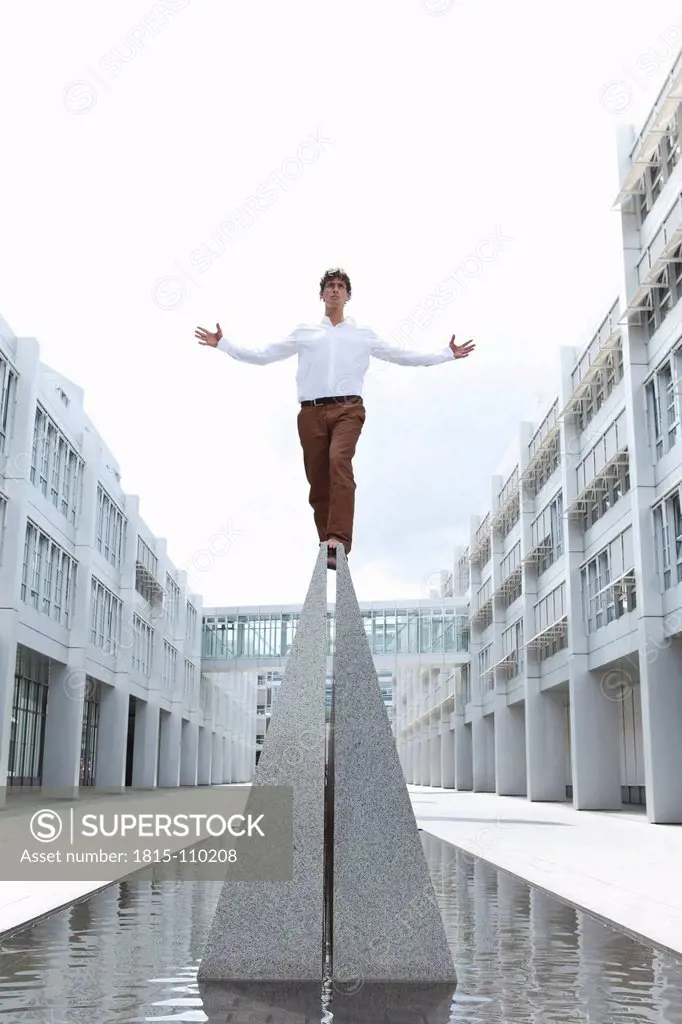 Germany, Bavaria, Young businessman standing on top with arm outstretched