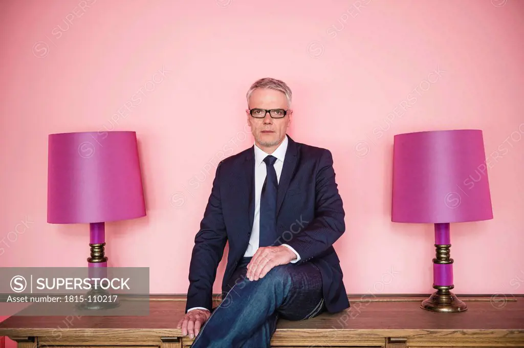 Germany, Stuttgart, Businessman sitting on sideboard with lamps, smiling, portrait