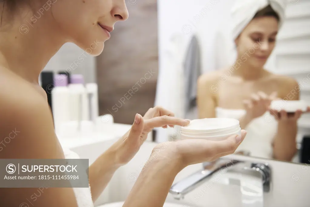 Young woman applying moisturizer in bathroom, partial view