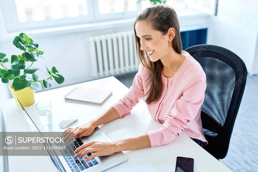 Smiling young woman working on laptop in home office