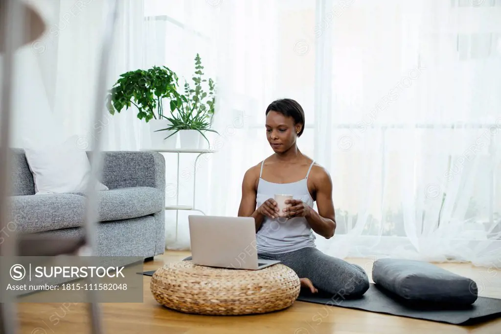 Woman sitting on gym mat at home using laptop