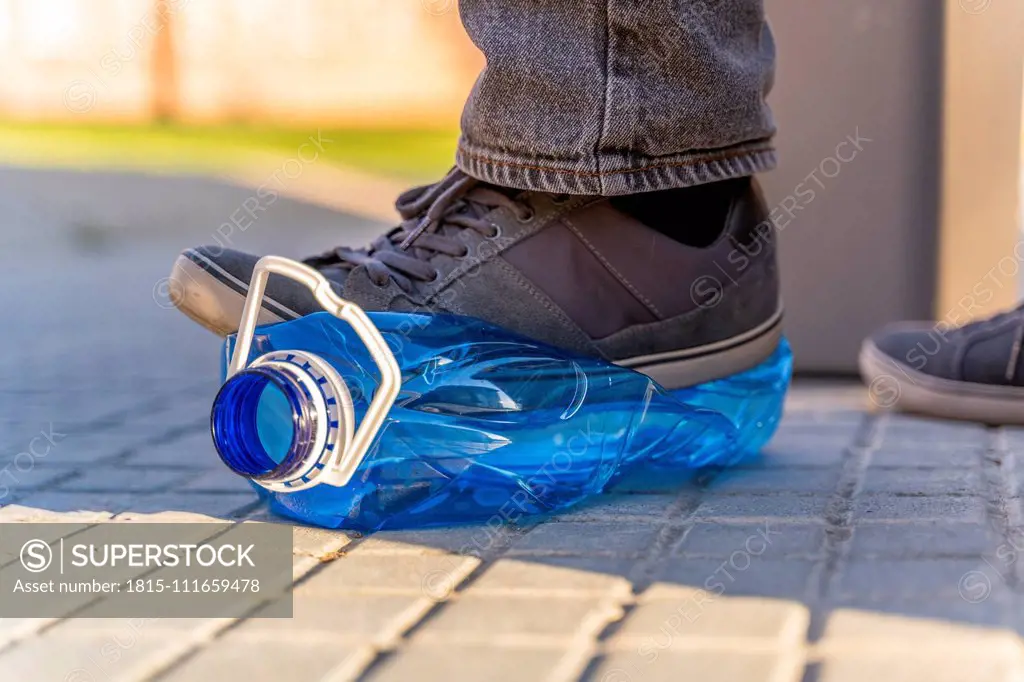 Close-up of man's feet sqashing plastic bottle for recycling