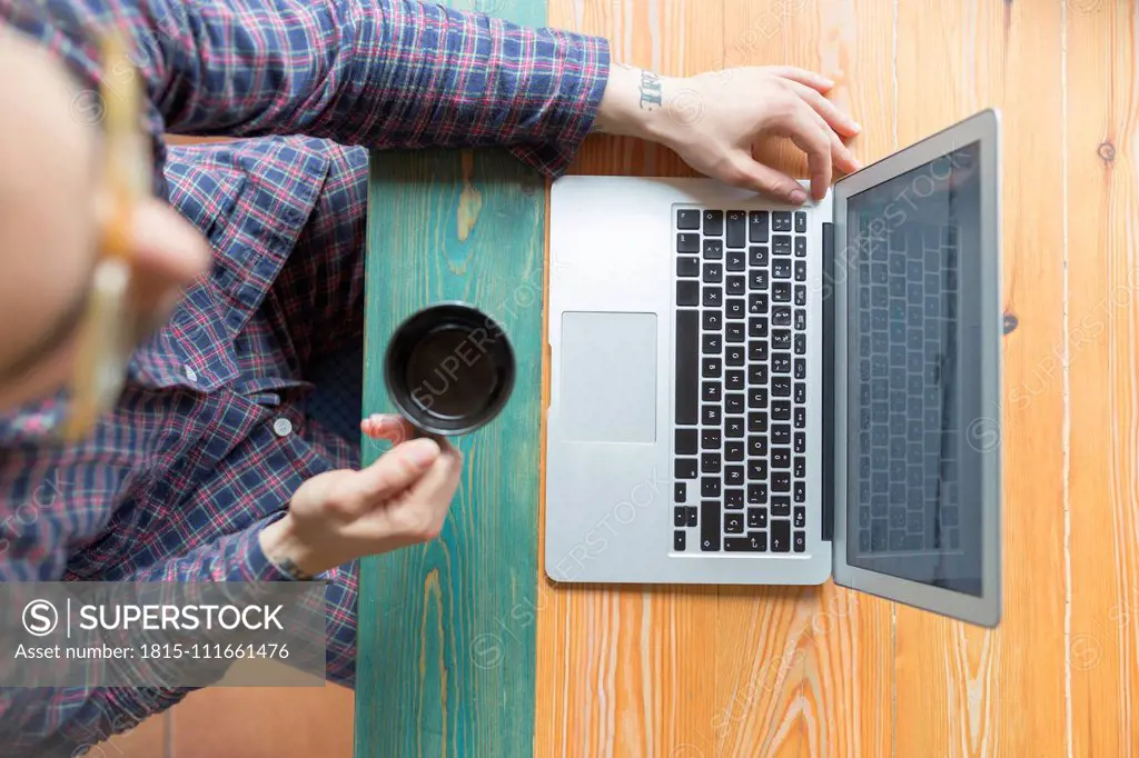 Man wearing pyjama sitting with coffee cup in front of laptop