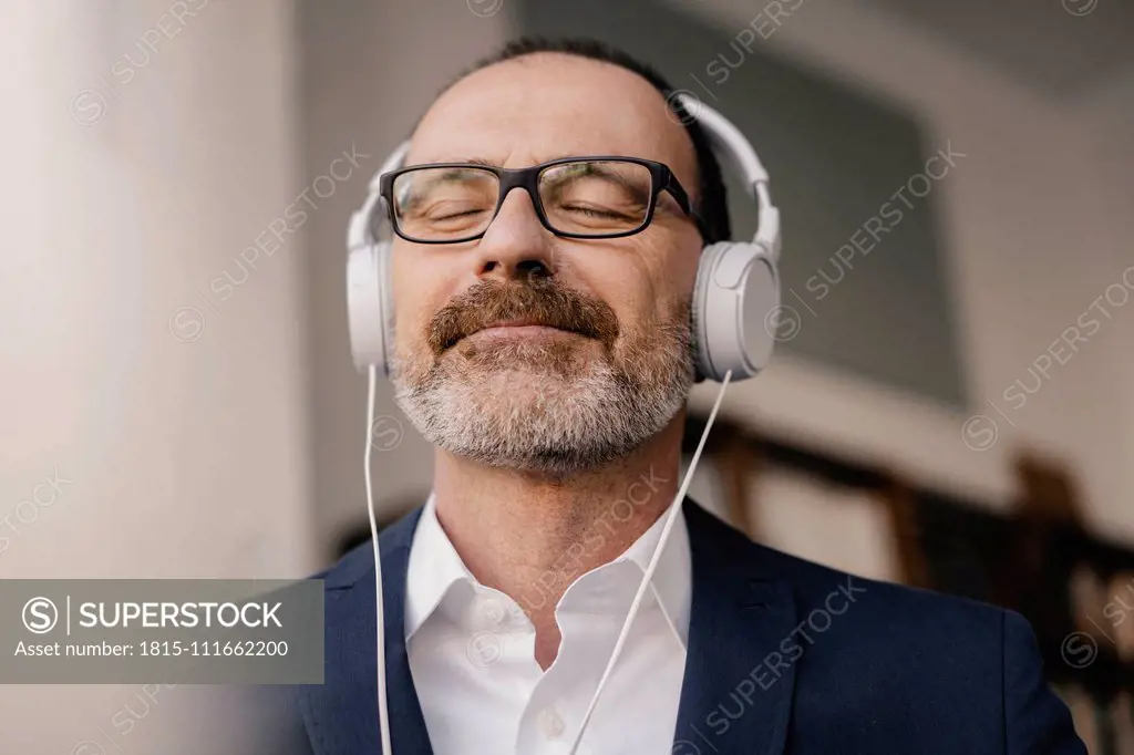 Mature businessman with closed eyes listening to music with headphones