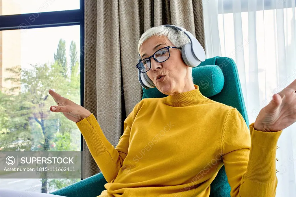 Senior woman sitting in armchair, listening music with headphones