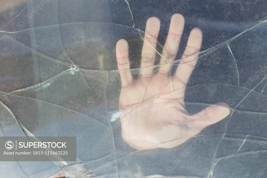 Hand of a young man behind broken windscreen on a scrapyard
