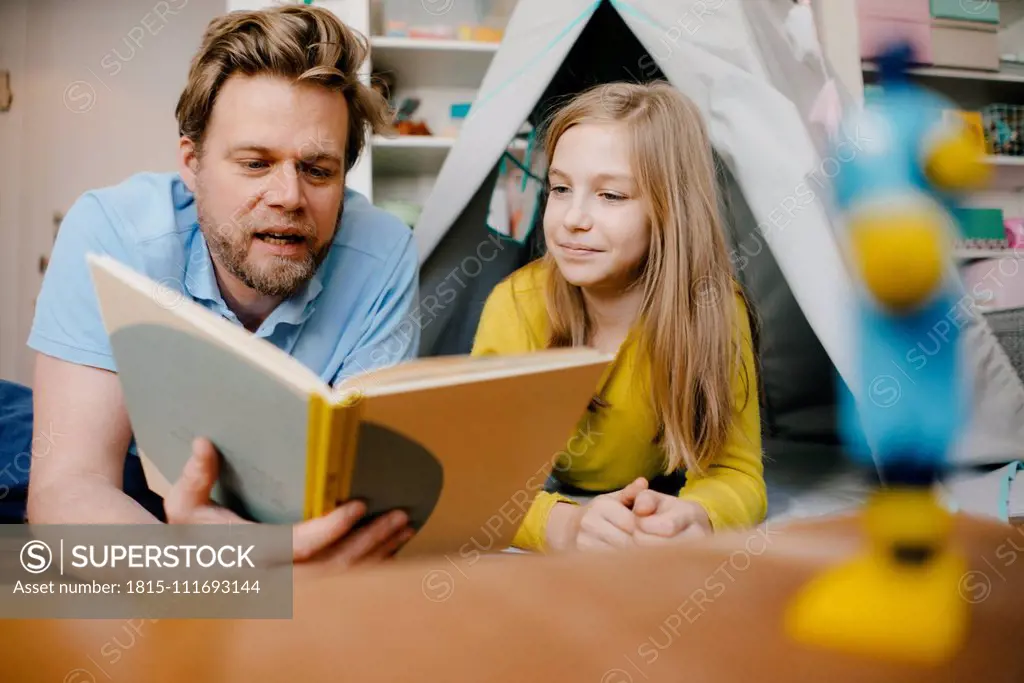 Father and daughter at home reading book in children's room