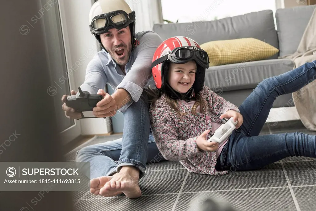 Young man and little girl wearing biker helmets, playing racing game with gaming consoles