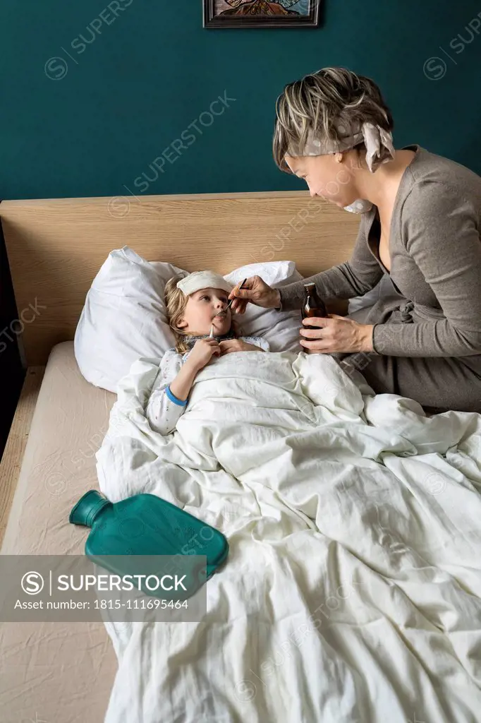 Mother giving medicine to sick daughter lying in bed