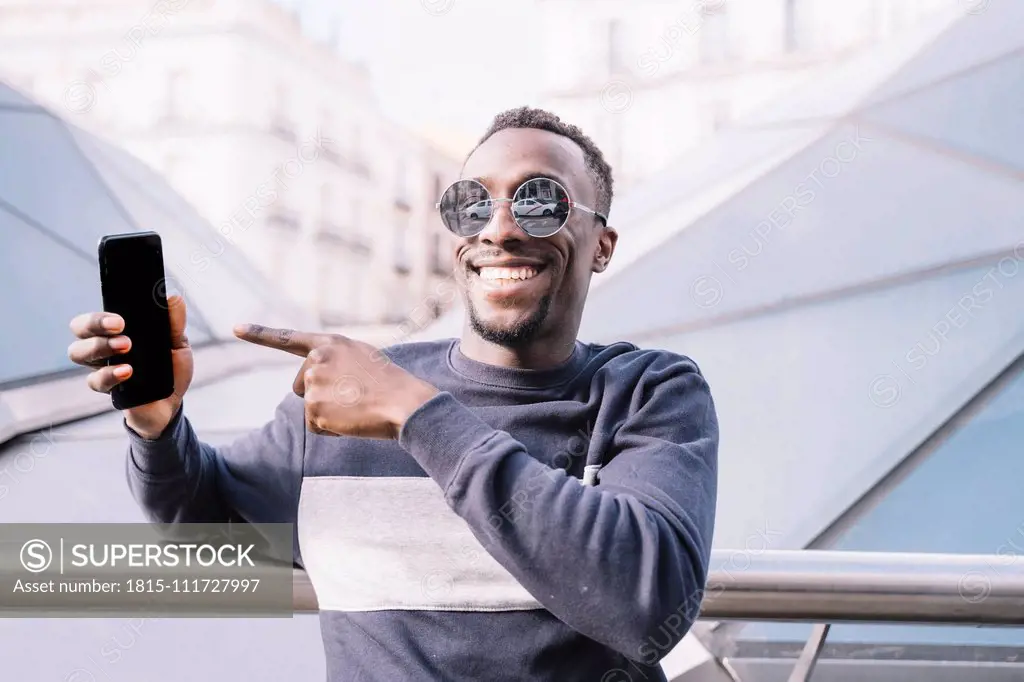 Spain, Madrid, portrait of happy young man showing his mobile phone