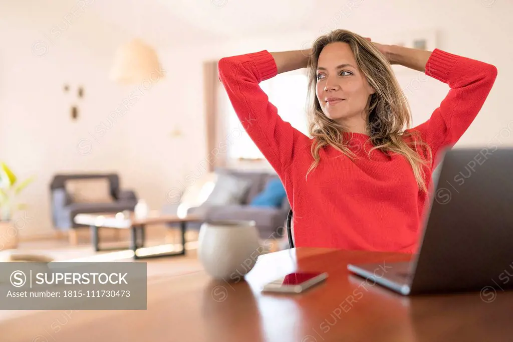 Woman sitting at dining table at home having a break from her work at the laptop