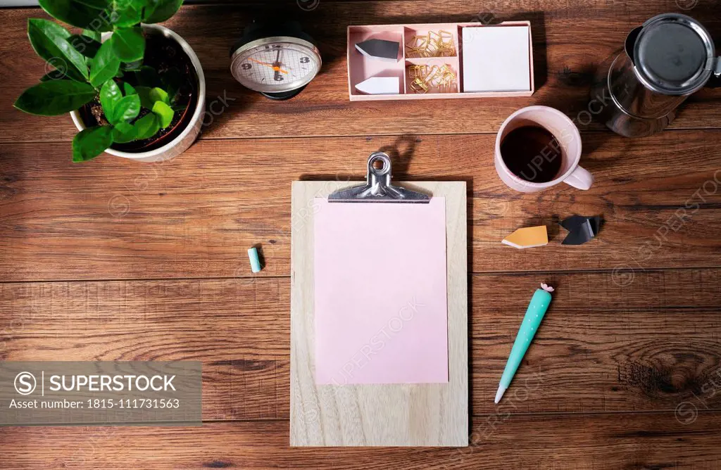 Clip board with blank pink paper, coffee mug and other utensils on desk at home office, top view