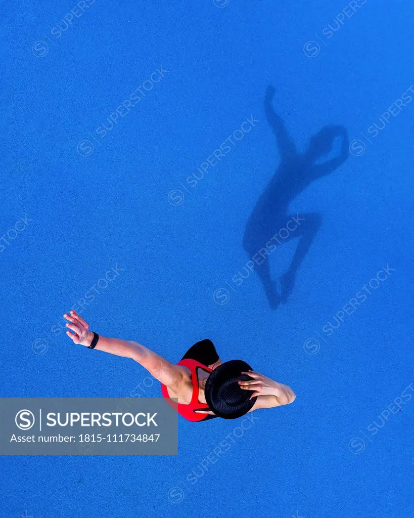 Jumping young woman and her shadow on blue background, top view