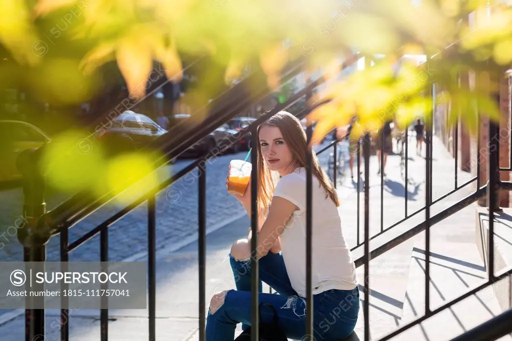 Young woman exploring New York City, sitting on stairs, drinking coffee