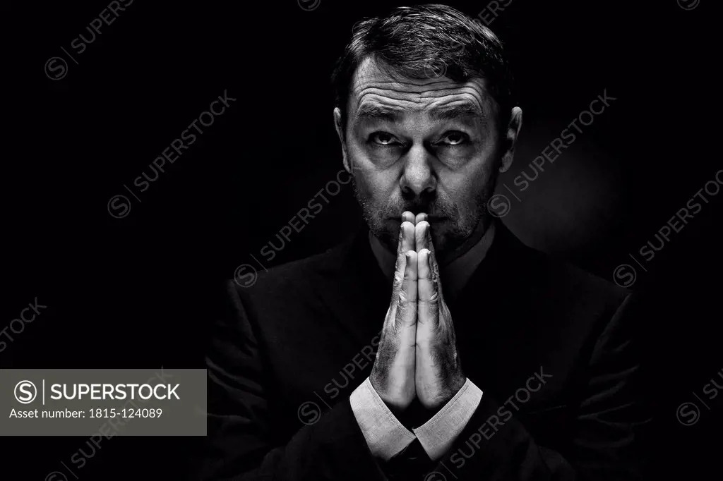Mature man in full suit praying against black background, close up