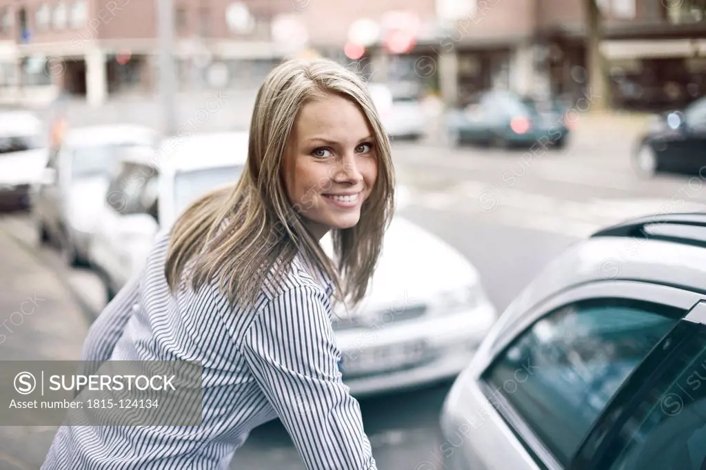 Germany, Duesseldorf, Young woman getting in to car, smiling, portrait