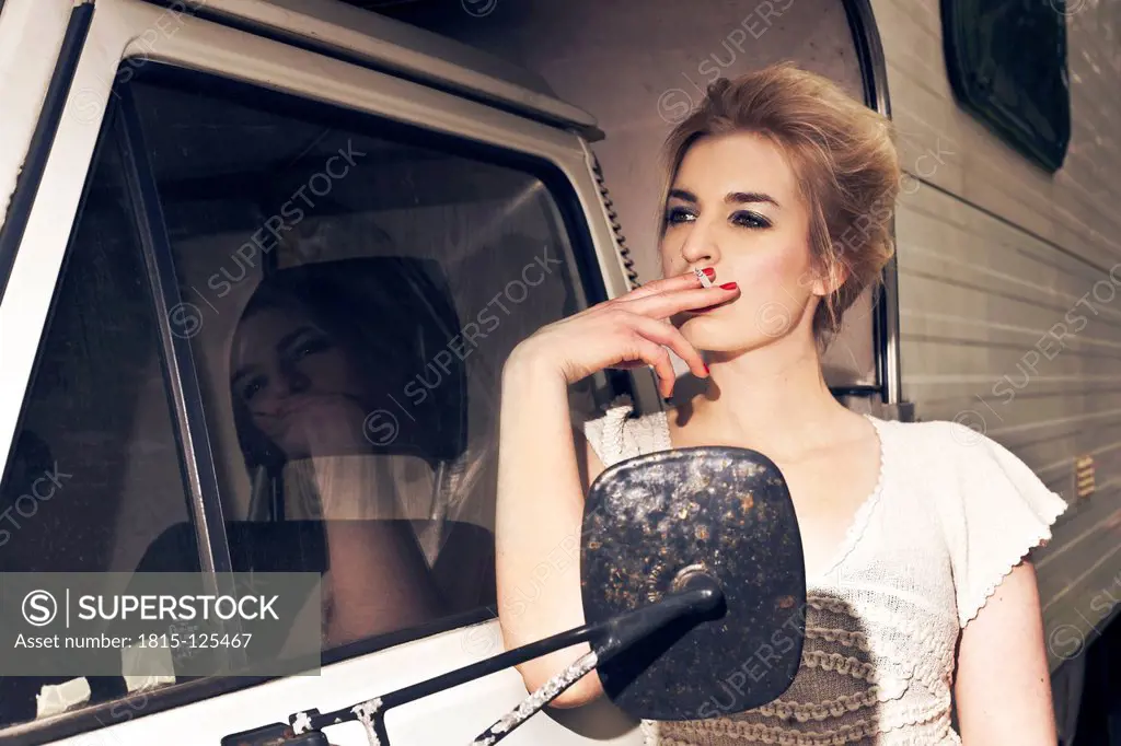 Germany, Berlin, Young woman smoking next to camping bus