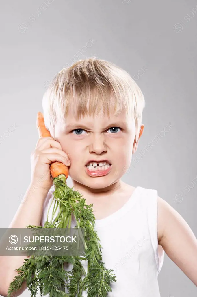 Boy imitating carrot as telephone, close up