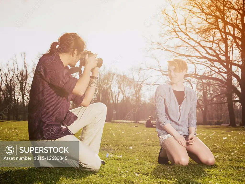 Young man photographing his girlfriend on a meadow