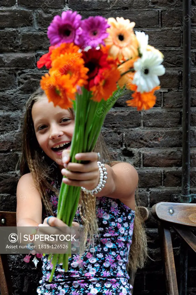 Netherlands, Girl holding flowers in front of brick wall, smiling