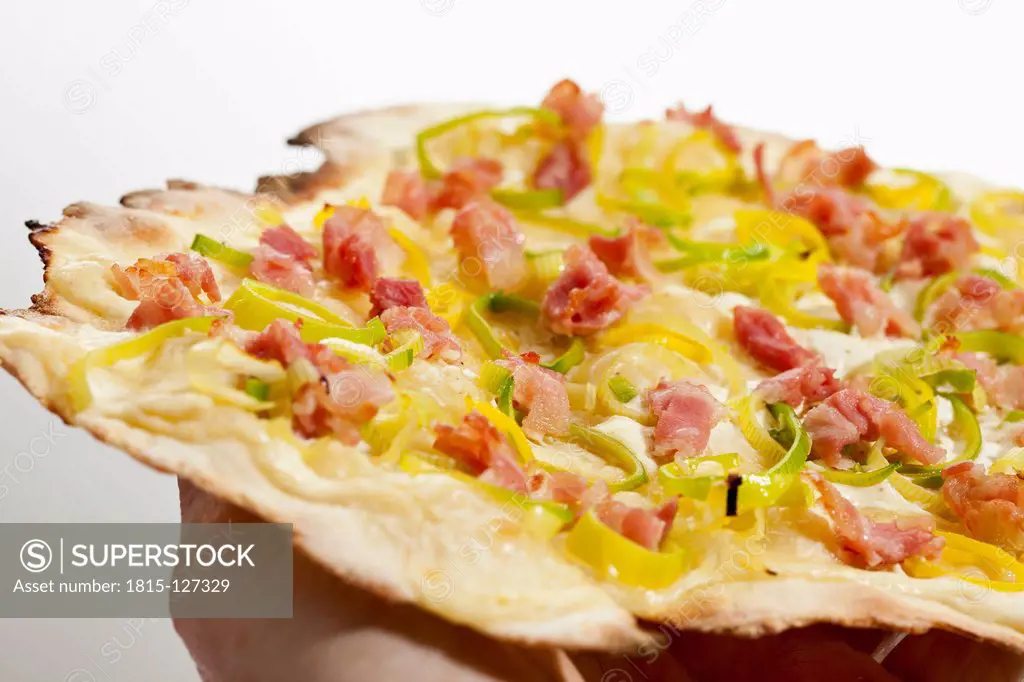 Human hand holding tarte flambee with onion and leeks, close up