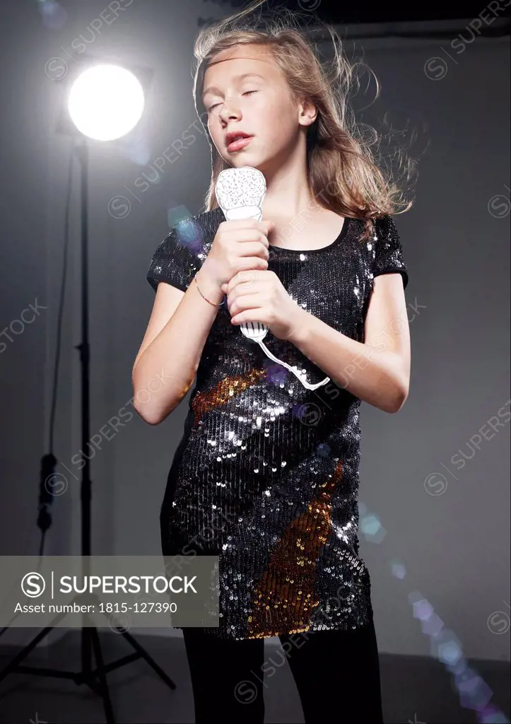 Girl singing in paper microphone against grey background