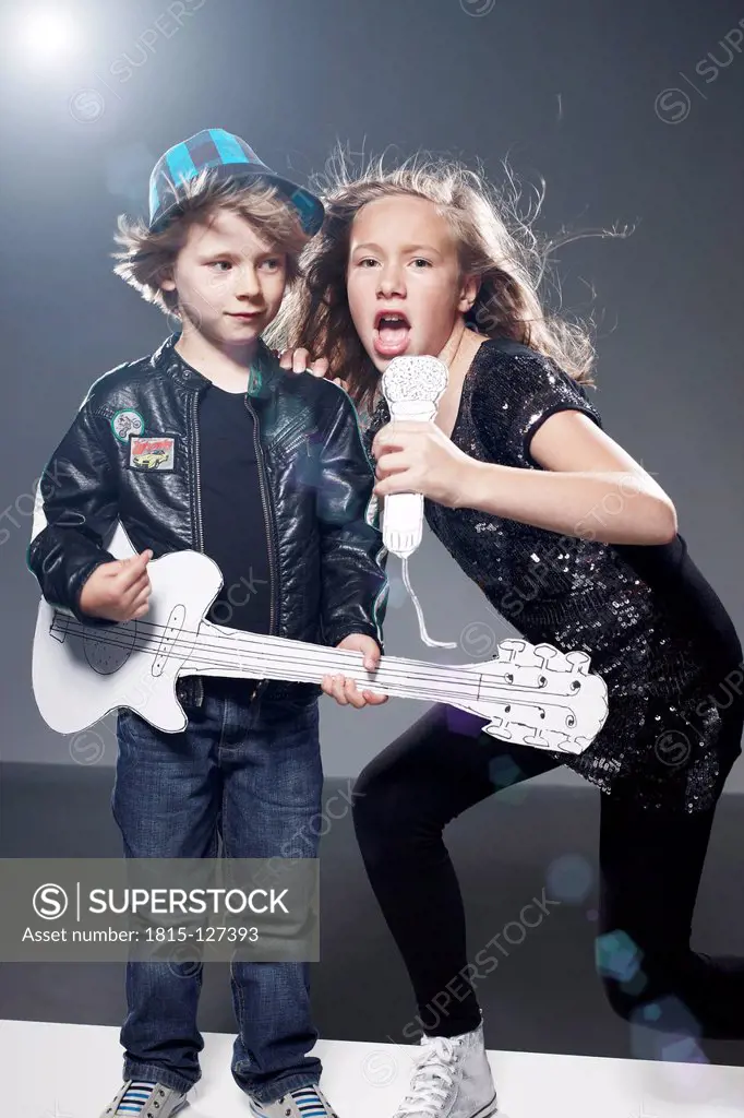 Girl and boy playing band on stage with paper guitar and microphone