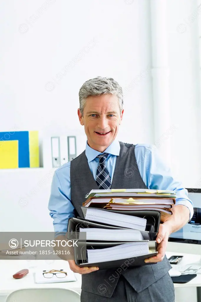 Germany, Businessman holding stack of files, smiling