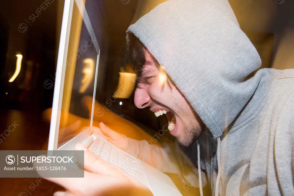 Germany, North Rhine Westphalia, Cologne. Young man screaming at his laptop