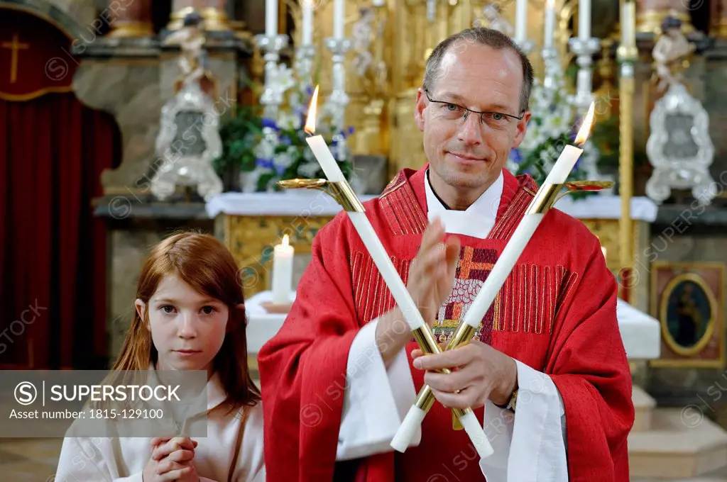 Germany, Bavaria, Priest holding candles for blessing of throats while altar server standing with hands clasped in church
