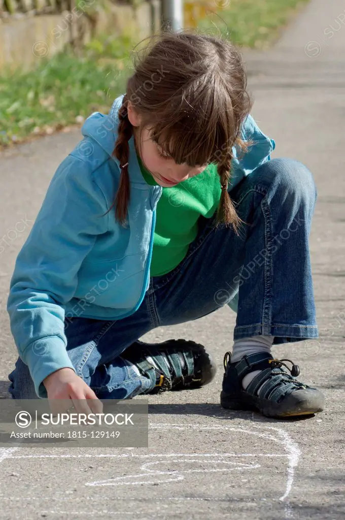 Germany, Tuebingen, Girl drawing hopscotch on street with chalk