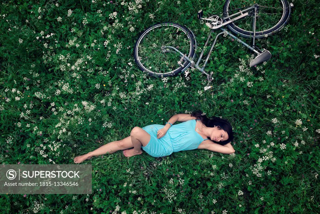 A young woman in a blue dress lying on a summer meadow, beside her, an old vintage bicycle
