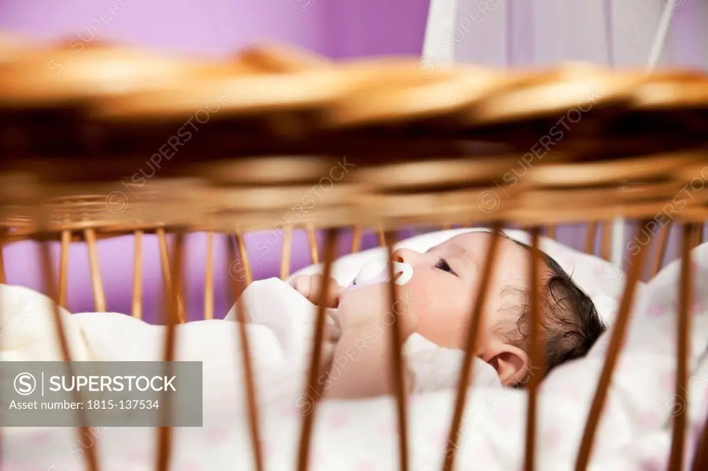 Baby girl lying in wicker crib, close up