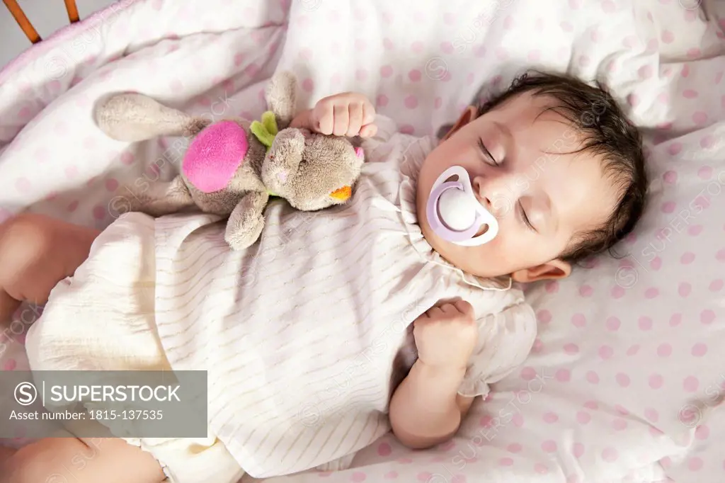 Baby girl sleeping in wicker crib with toy