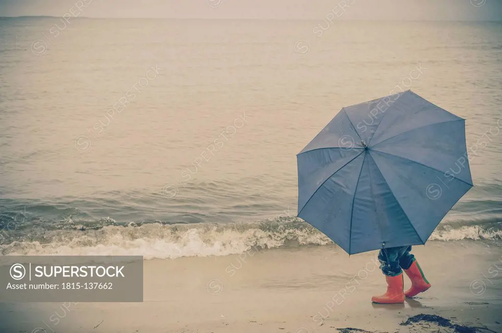 Germany, Mecklenburg Western Pomerania, Boy with umbrella in rain at baltic sea