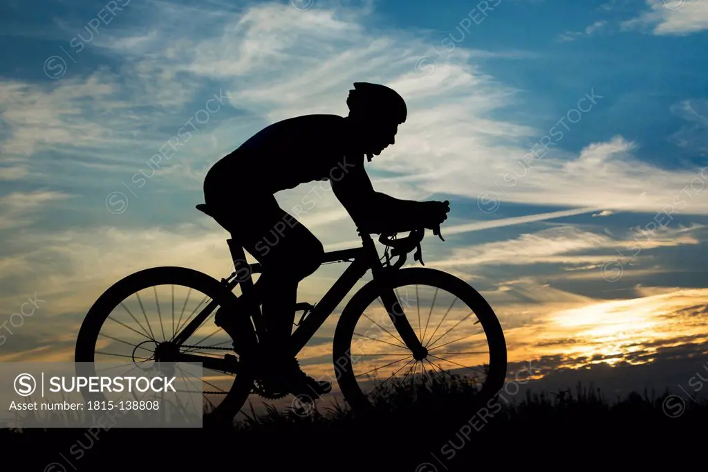 Germany, Mature man riding bicycle in sunset