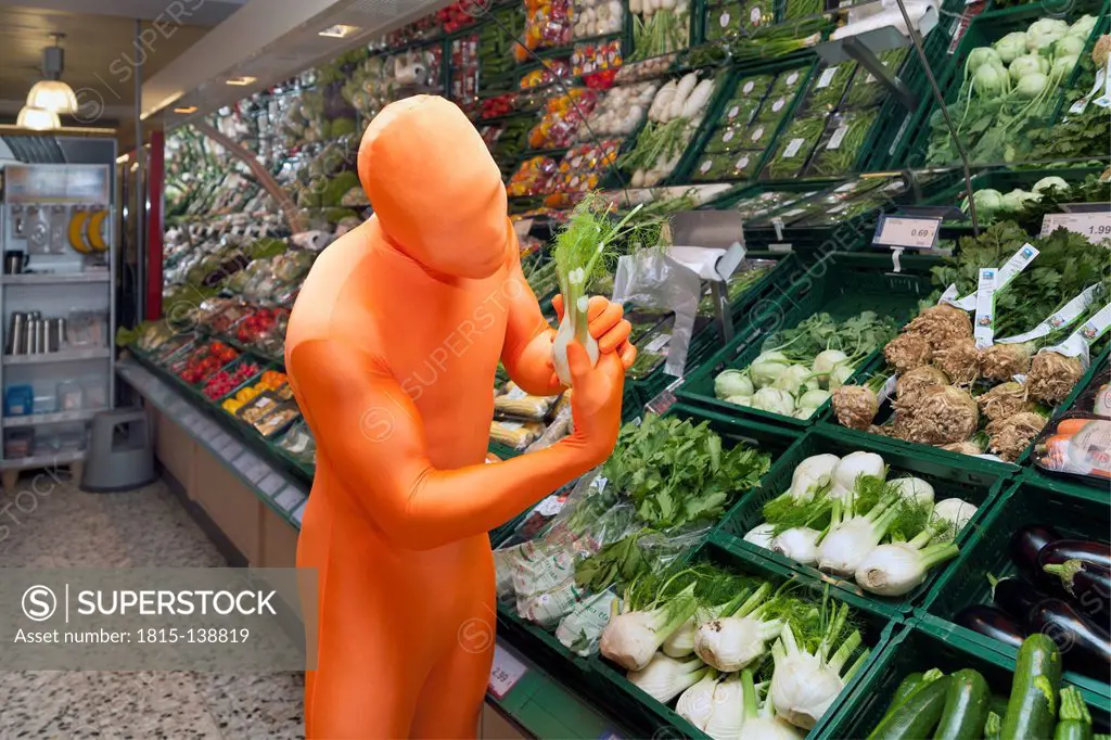 Germany, Mature man dressed in orange morphsuit looking at fennel in supermarket