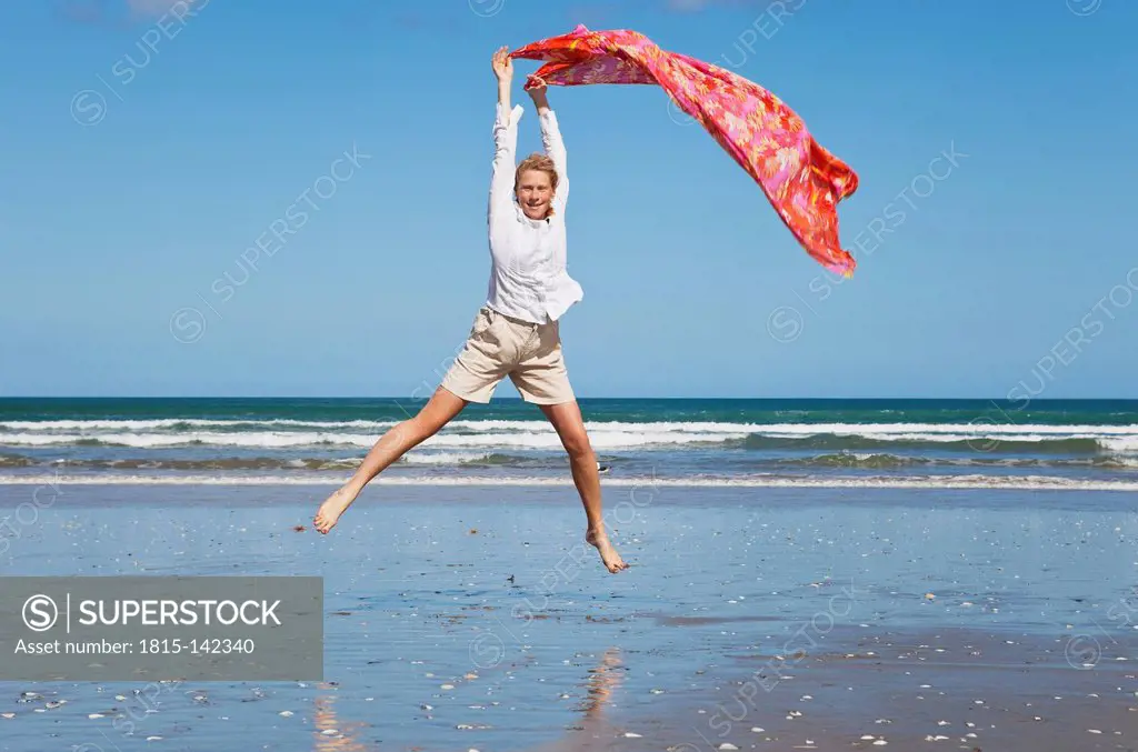 New Zealand, Mature woman jumping at Ninety Mile Beach