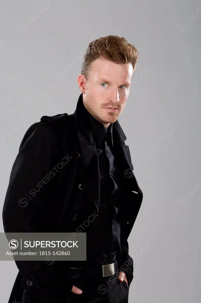 Mid adult man in black coat standing against grey background