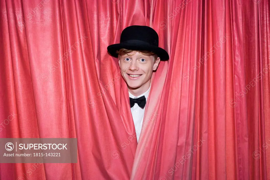 Germany, Young magician behind curtain, smiling
