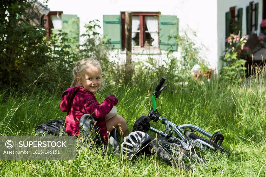 Germany, bavaria, Inzell, Girl sitting in meadow with bicycle, smiling