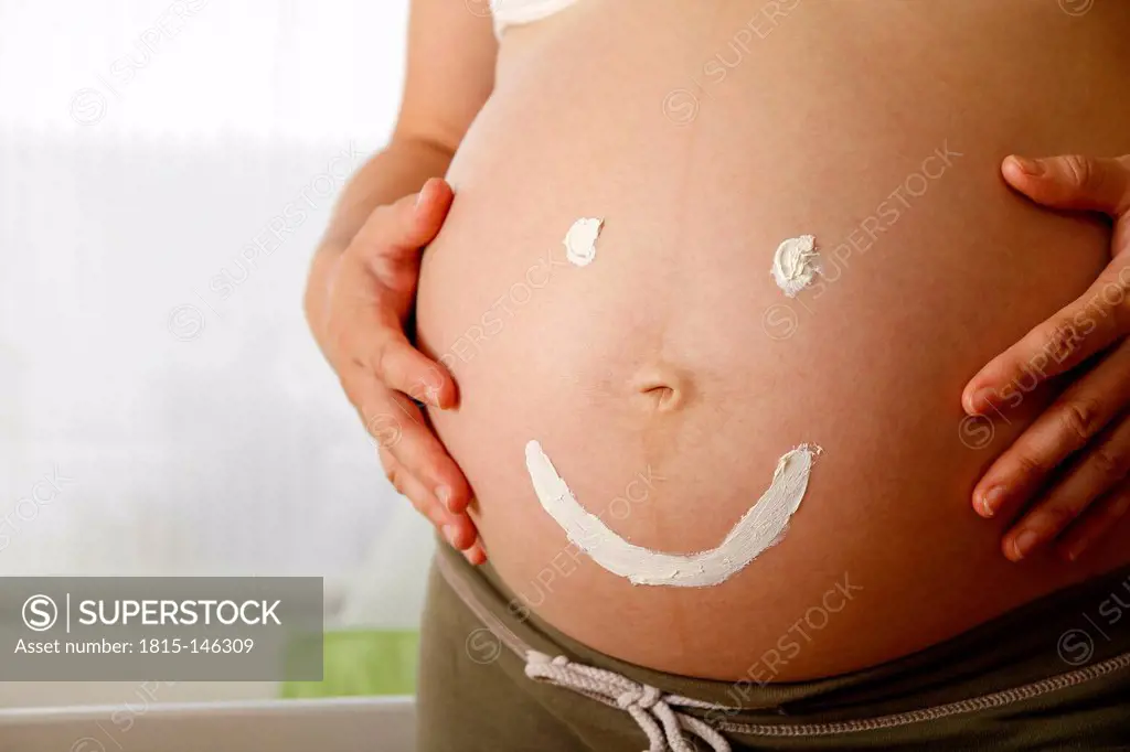 Pregnant woman with happy smiley painted on belly