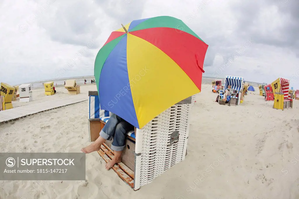 Germany, Lower Saxony, East Frisia, Langeoog, woman with open umbrella sitting on a roofed wicker beach chair