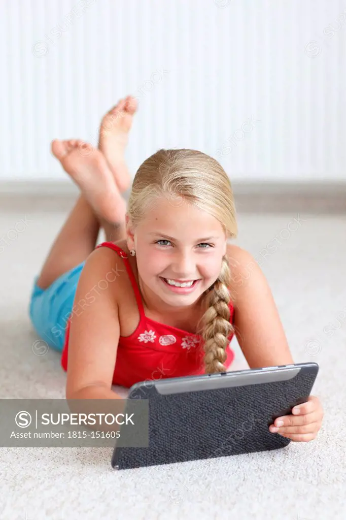 Smiling blond girl using digital tablet on the floor