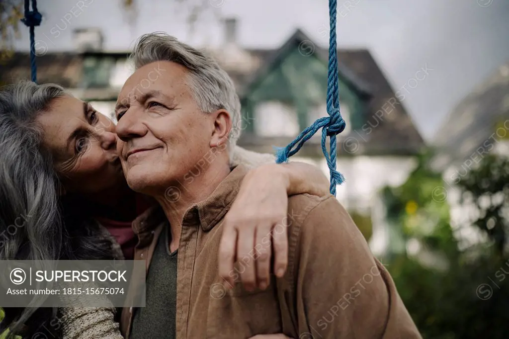 Happy woman hugging an kissing senior man on a swing in garden