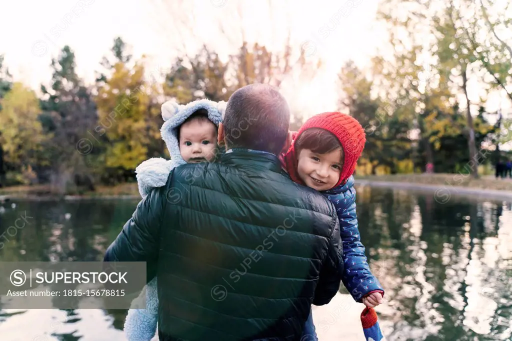 Portrait of two little girls on father's arms in front of a lake at sunset
