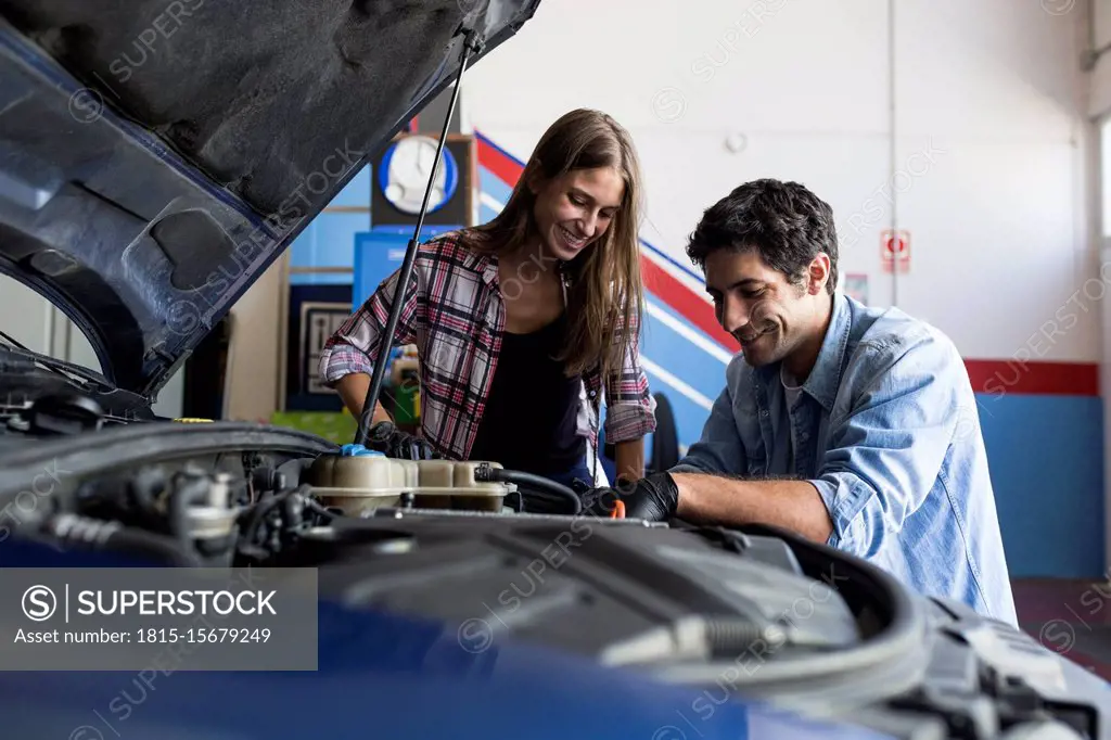 Cheerful man and young woman working together on car repair service and  fixing car engine - SuperStock