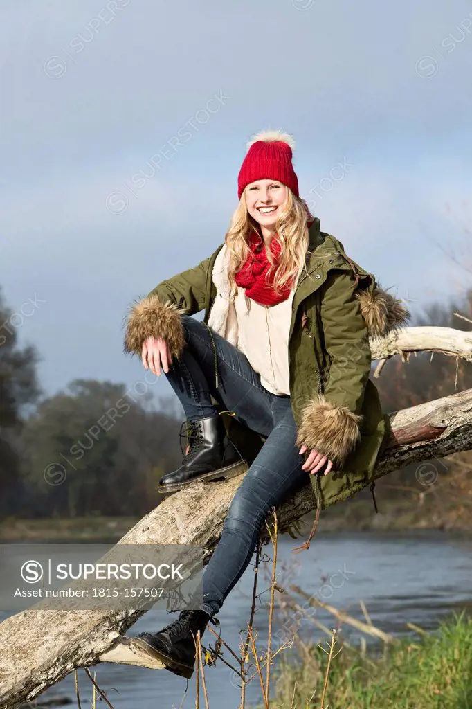 Smiling young woman sitting at tree trunk