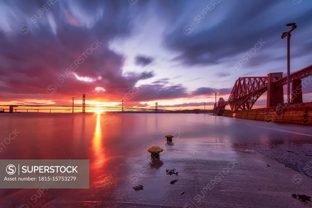UK, Scotland, South Queensferry, Forth Bridge at dramatic sunset with Forth Road Bridge and Queensferry Crossing in distant background